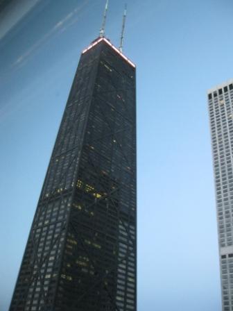 a tall black skyscraper with a red top with John Hancock Center in the background