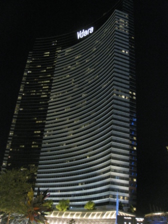 a tall building with lights on with Vdara in the background