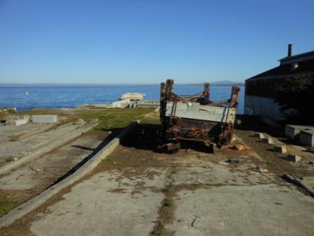 a rusty metal object on the ground next to a body of water