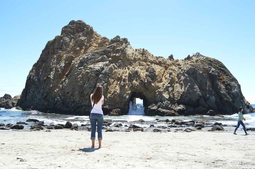 a woman standing on a beach looking at a cave
