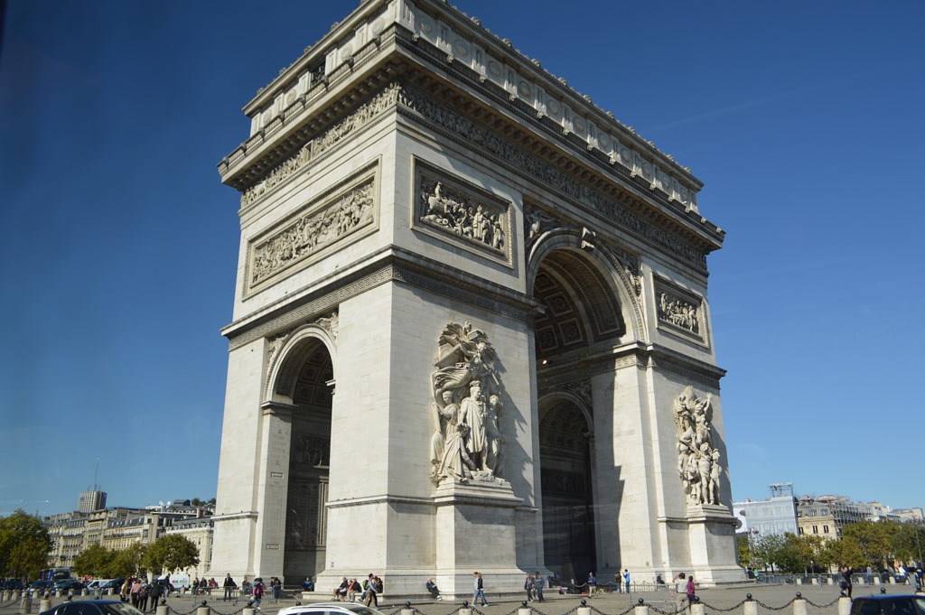 a large stone arch with statues on it with Arc de Triomphe in the background