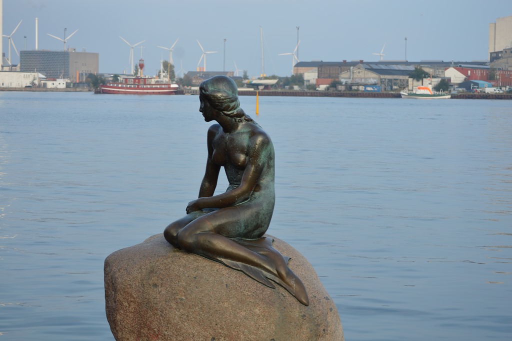 a statue of a woman sitting on a rock by water