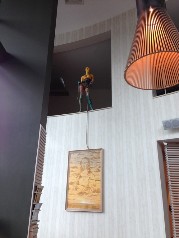 a mannequin on a ledge with a painting from the ceiling