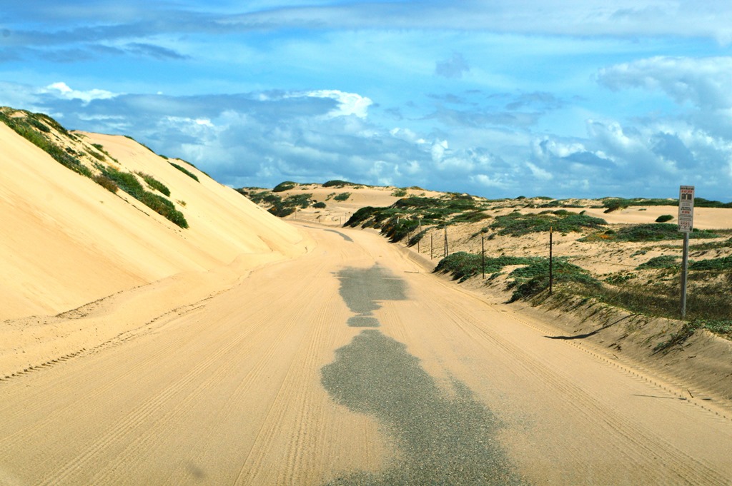 a road with sand hills and blue sky