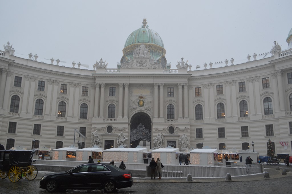a large white building with a dome and people walking around with Hofburg in the background