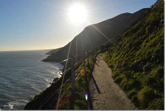 a path on a hill with a fence and a body of water