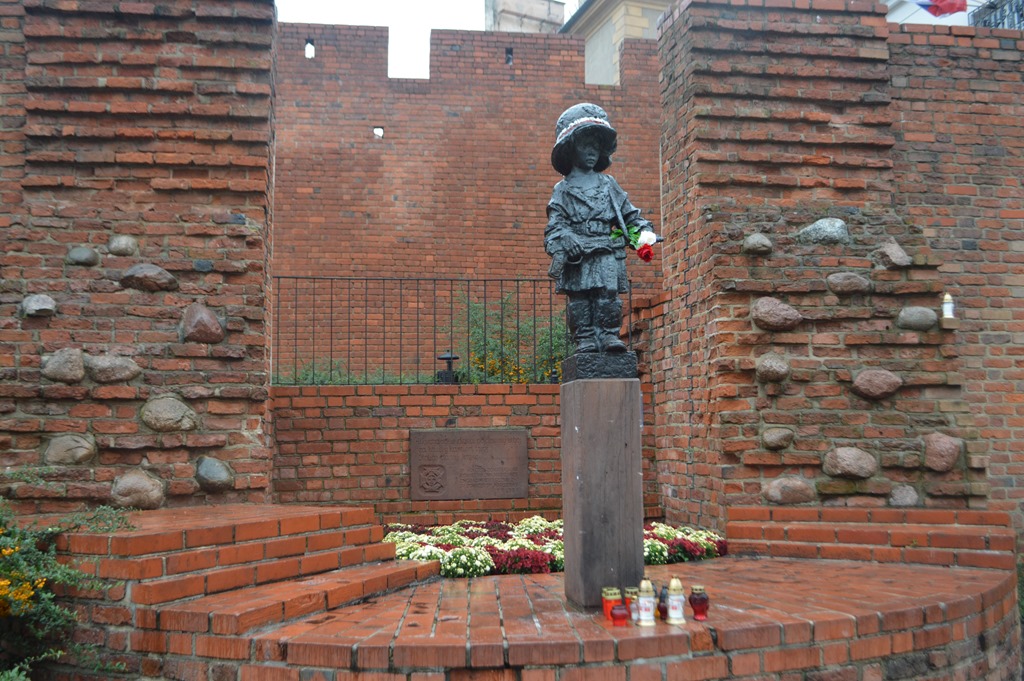 a statue of a child with flowers in front of a brick wall