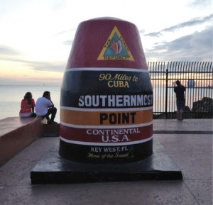 a large sign on a concrete wall with Southernmost point buoy in the background