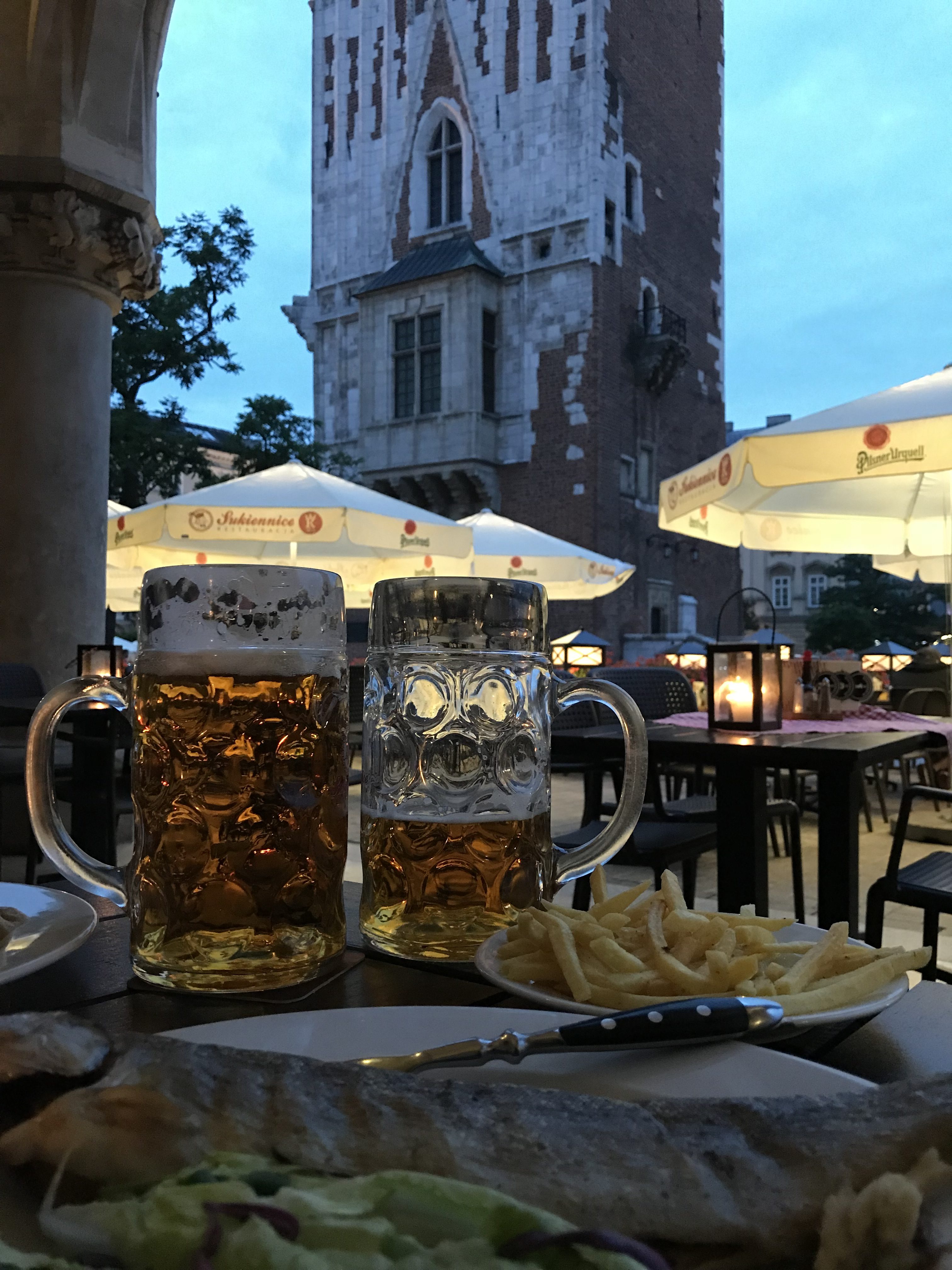 two glasses of beer and fries on a table outside