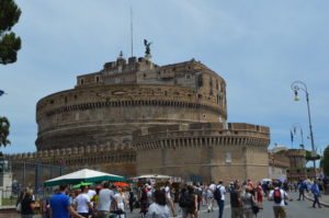 a large stone castle with people walking around with Castel Sant'Angelo in the background