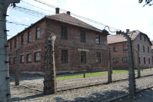 a brick building with a fence with Auschwitz concentration camp in the background