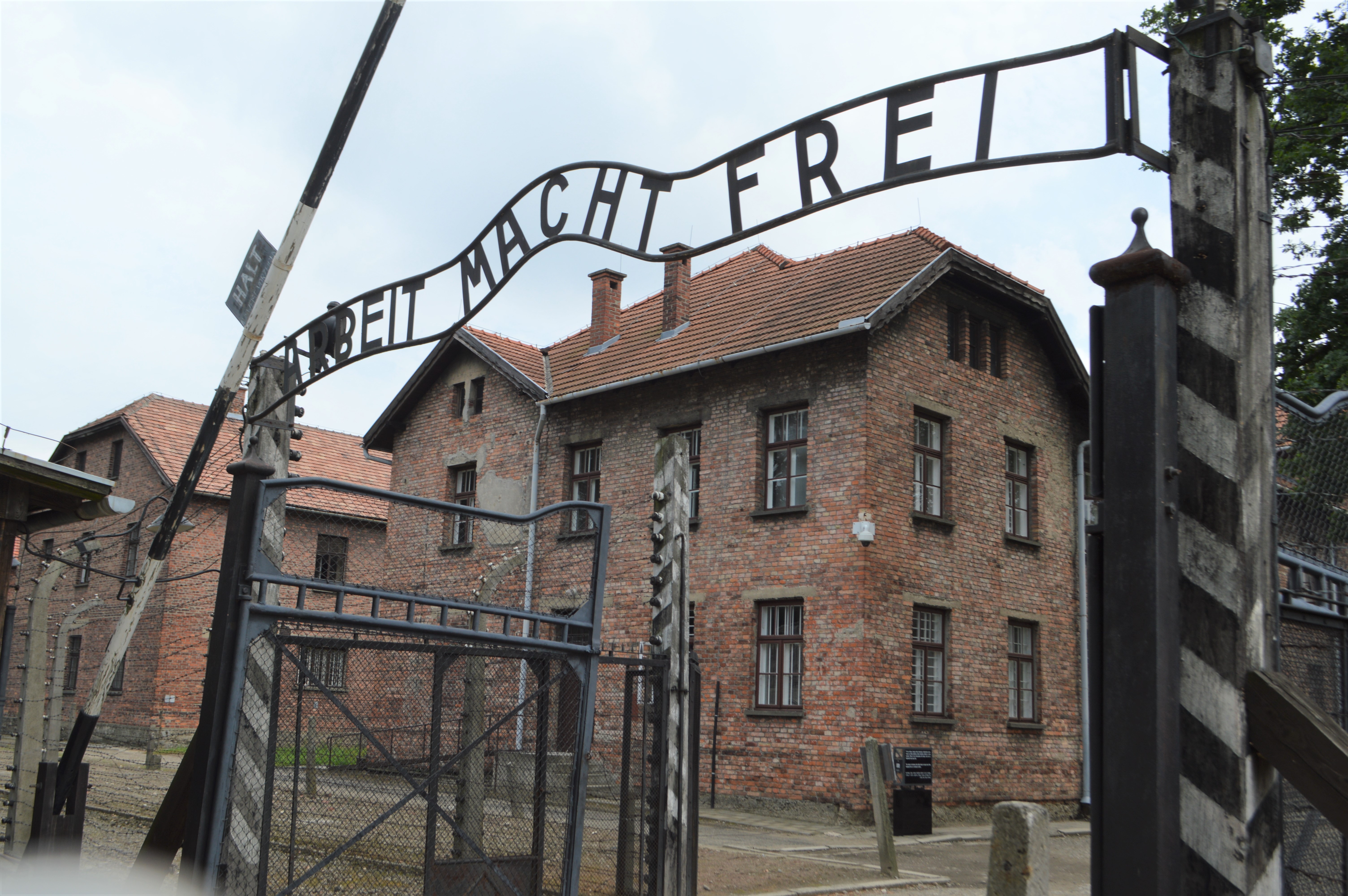 a gate with a brick building behind it with Auschwitz concentration camp in the background