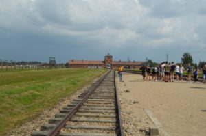 a group of people standing next to train tracks with Auschwitz concentration camp in the background