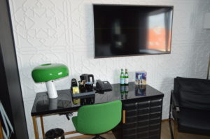 a desk with a green chair and a television on the wall