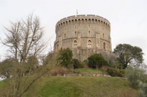 a round stone building with trees and grass with Windsor Castle in the background