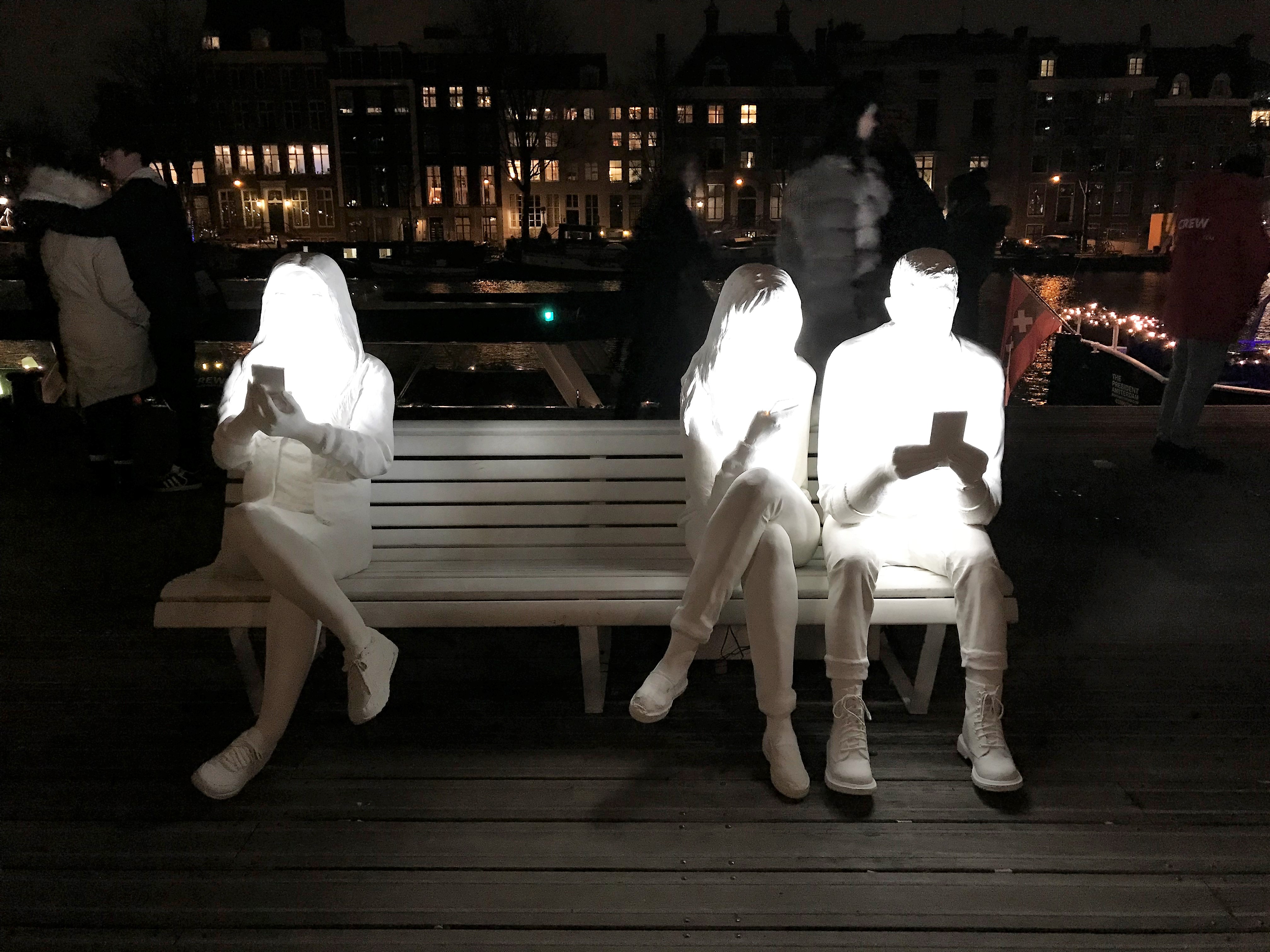 people wearing white clothing sitting on a bench with their faces turned on