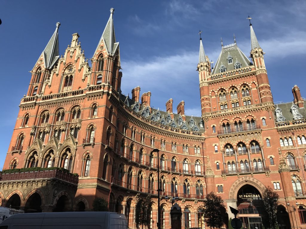 a large brick building with pointed towers with St Pancras railway station in the background