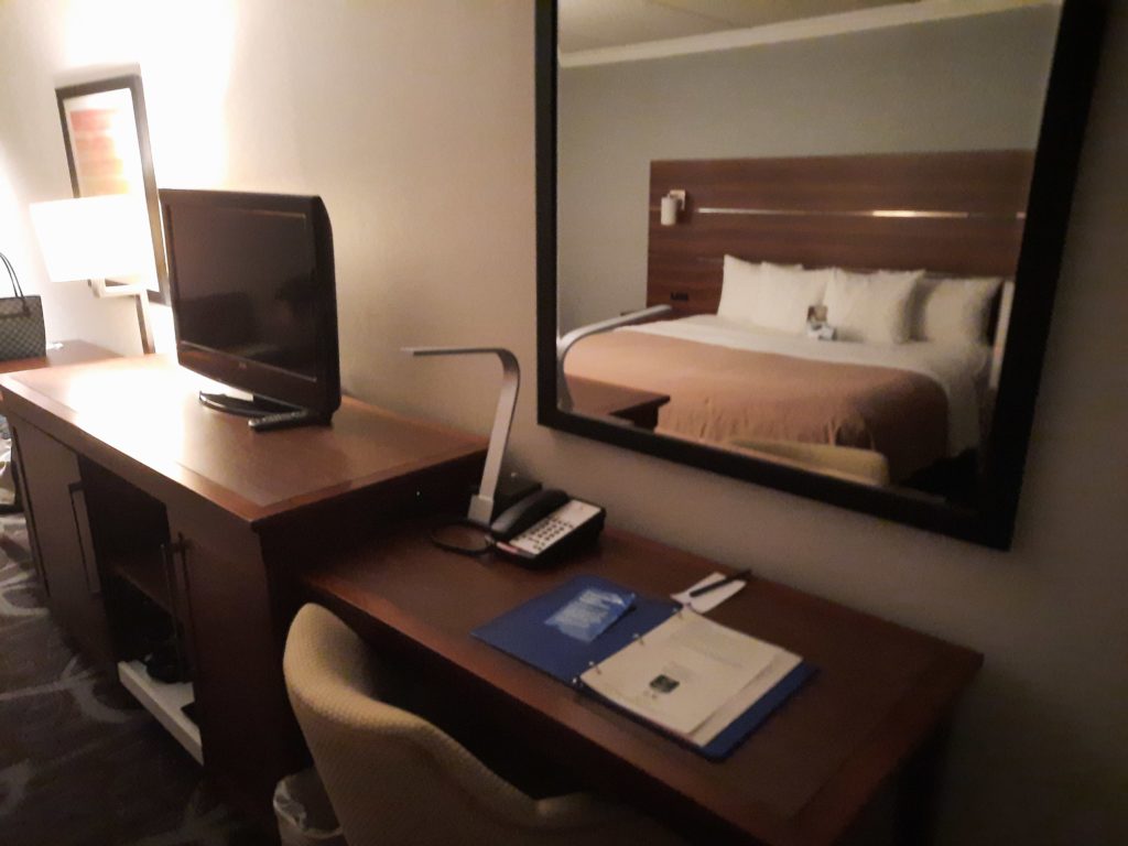 a desk with a television and a mirror in a hotel room