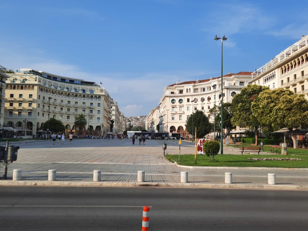 a street with buildings and trees with Thessaloniki in the background