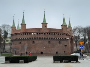 a brick building with green spires with Kraków Barbican in the background