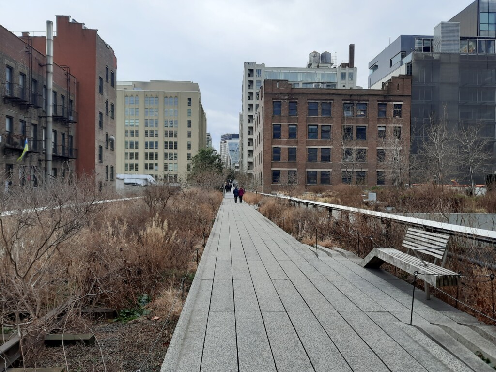 a walkway with benches and buildings in the background with High Line in the background