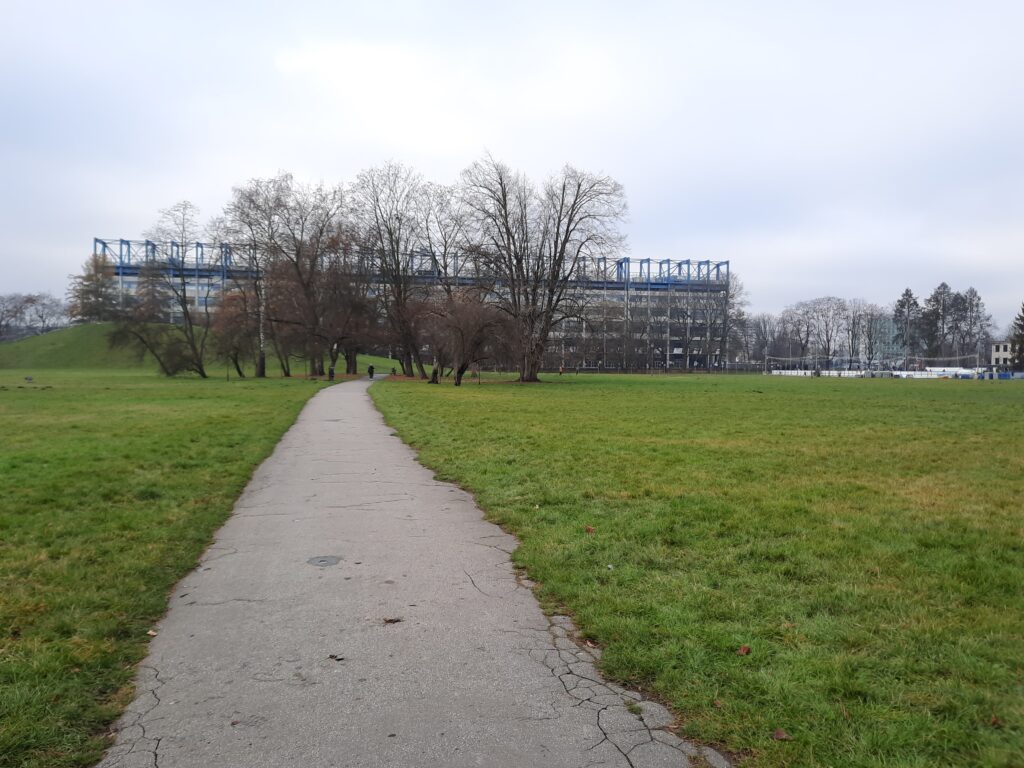 a path in a park with trees and a building in the background