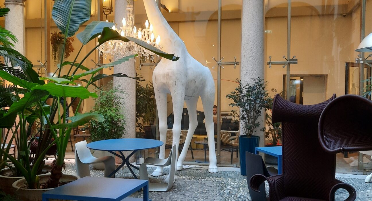 a large white statue of a giraffe in a room with blue chairs and tables