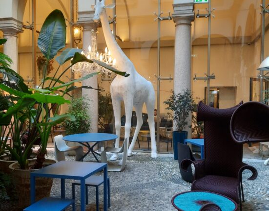 a large white statue of a giraffe in a room with blue chairs and tables
