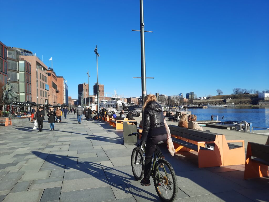 a woman on a bicycle on a sidewalk with people walking around