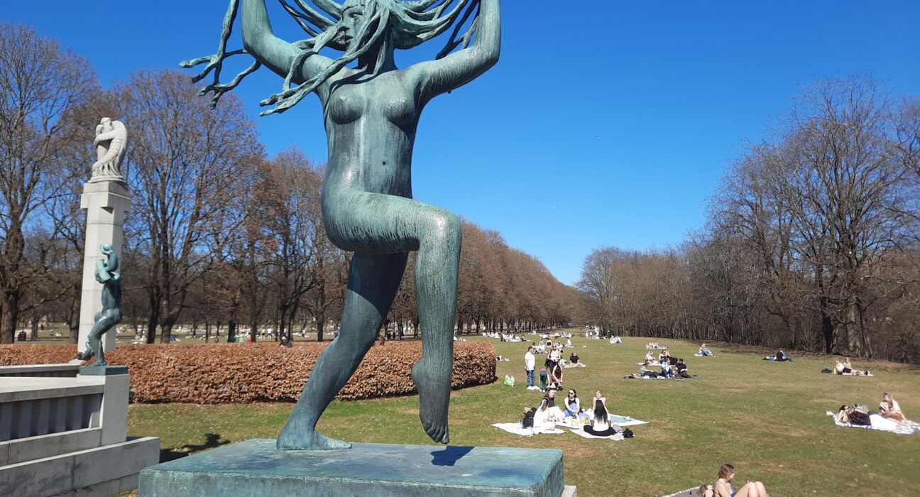 a statue of a woman with long hair and people in the grass