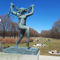 a statue of a woman with long hair and people in the grass