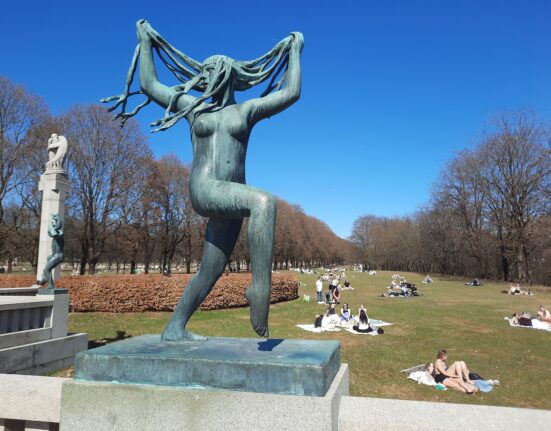 a statue of a woman with long hair and people in the grass